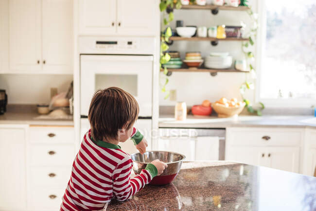 Мальчик опирается на кухонный прилавок перемешивая смесь для выпечки — стоковое фото