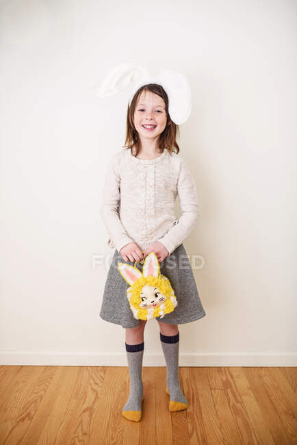 Retrato de una chica sonriente con orejas de conejo sosteniendo una bolsa de conejo - foto de stock
