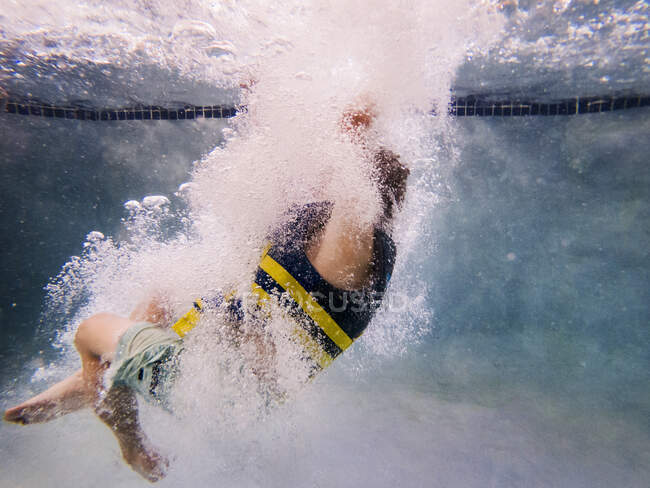 Підводний вигляд молодого хлопчика, який стрибає у басейн з рятувальною курткою — стокове фото