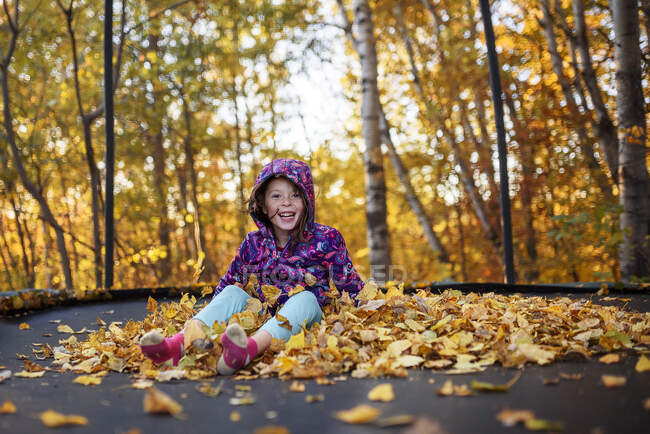 Menina sorridente sentada em uma pilha de folhas de outono em um trampolim, Estados Unidos — Fotografia de Stock