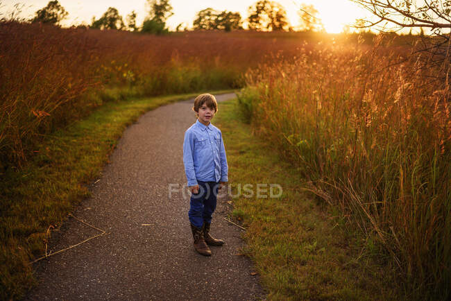 Хлопчик, що стоїть на стежці біля поля на заході сонця (США). — стокове фото