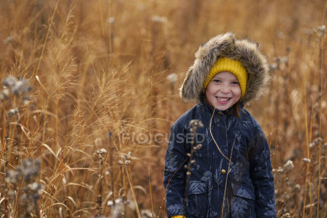 Portrait d'une fille souriante debout dans un champ mâchant un morceau d'herbe longue, États-Unis — Photo de stock