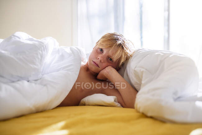 Menino deitado na cama encostado ao cotovelo — Fotografia de Stock