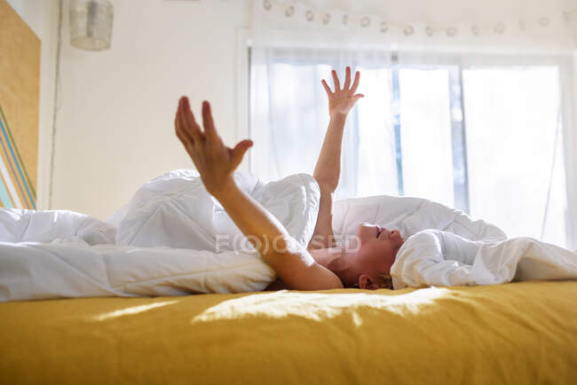 Boy lying in bed with his arms raised — Stock Photo