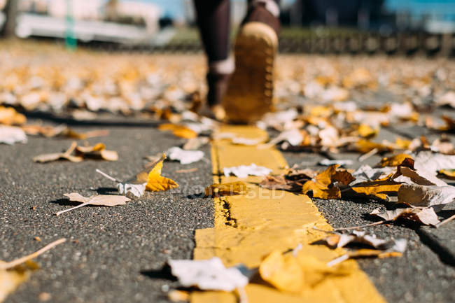 Frau läuft eine Straße entlang, die mit Herbstblättern bedeckt ist — Stockfoto