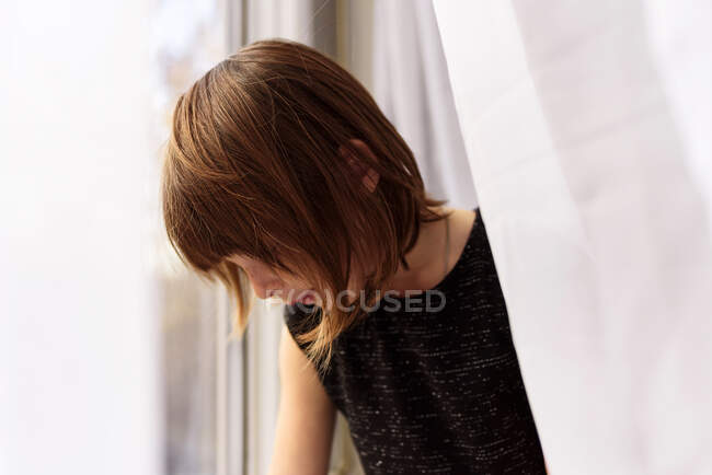 Retrato de uma menina atrás de uma cortina olhando para fora de uma janela — Fotografia de Stock