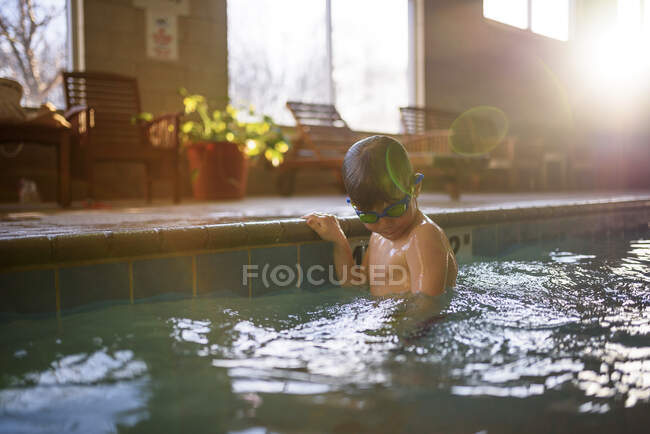 Niño aferrado al borde de una piscina - foto de stock