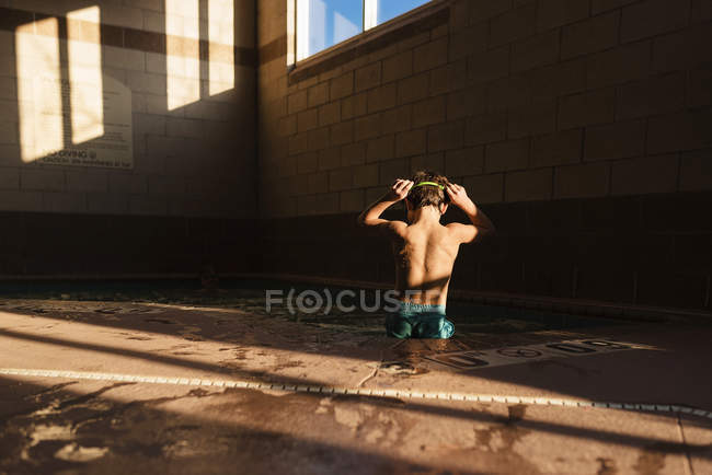 Niño de pie en una piscina ajustando sus gafas de natación - foto de stock