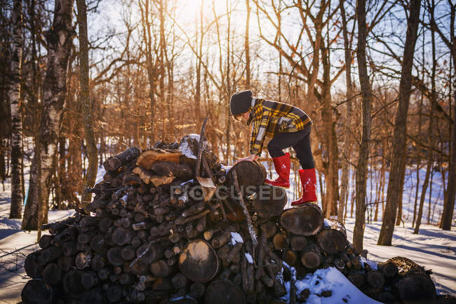 Boy climbing onto a woodpile in the snow, United States — Stock Photo