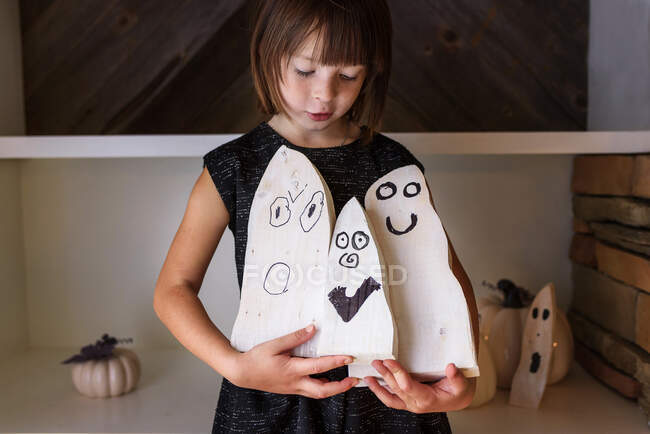 Smiling girl holding three wooden ghost decorations for Halloween — Stock Photo