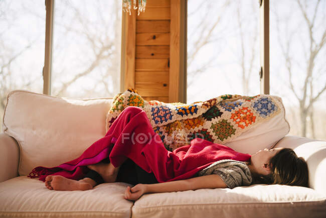 Ragazza sdraiata su un divano sotto una coperta — Foto stock
