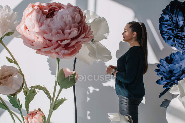 Retrato de uma mulher de pé ao lado de flores artificiais gigantes — Fotografia de Stock