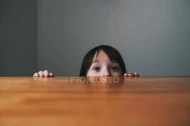 Mädchen versteckt sich hinter einem Tisch — Stockfoto