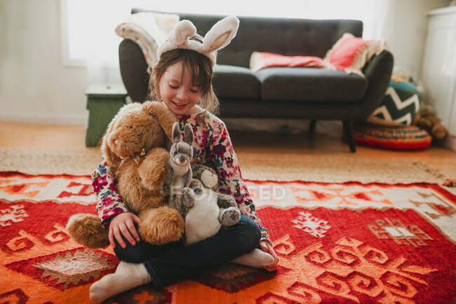Портрет дівчини у вухах кролика, що сидить на підлозі, тримає м'які іграшки — стокове фото