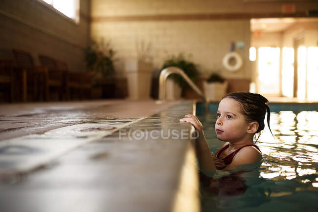 Chica aferrada al borde de una piscina - foto de stock