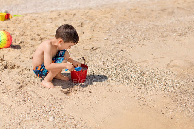 Garçon remplissant un seau de sable sur la plage, Grèce — Photo de stock