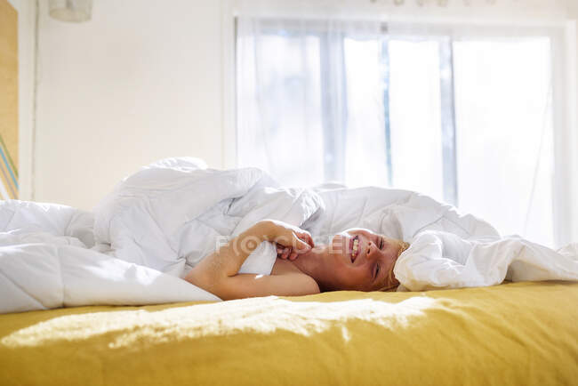 Хлопчик лежить у ліжку сміється — стокове фото