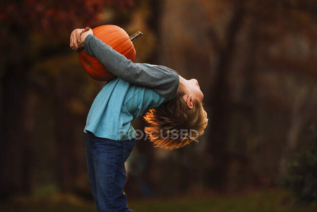 Boy standing in garden leaning back while holding a pumpkin, United States — Stock Photo