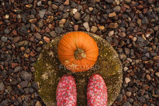 Overhead view of a woman's feet standing next to a pumpkin — Stock Photo