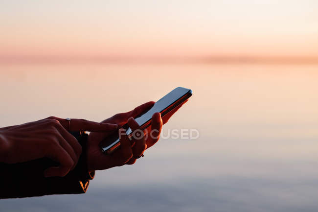 Donna in piedi all'aperto utilizzando un telefono cellulare al tramonto — Foto stock