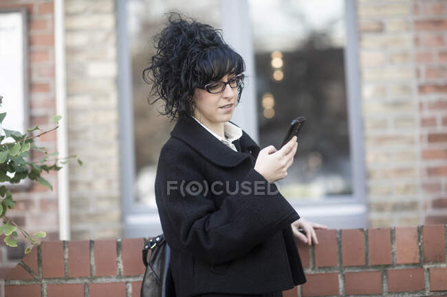 Mujer sonriente parada al aire libre usando su teléfono móvil, Alemania - foto de stock