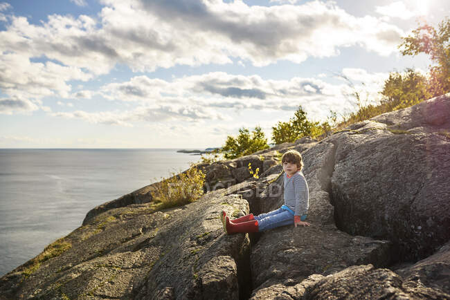Garçon assis sur des rochers au bord d'un lac, parc provincial du lac Supérieur, États-Unis — Photo de stock