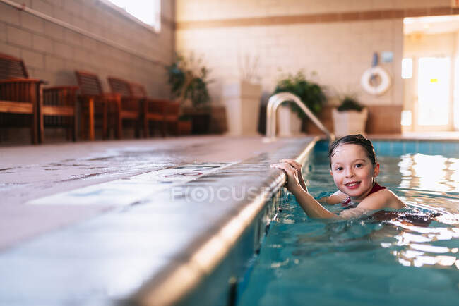 Sonriente chica aferrándose al borde de una piscina - foto de stock