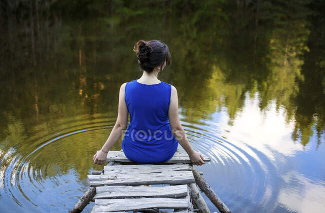 Rear view of a woman in a blue dress sitting on a wooden pier by a lake, Bulgaria — Stock Photo