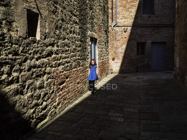 Ragazza che cammina in un vicolo illuminato dal sole, Toscana, Italia — Foto stock