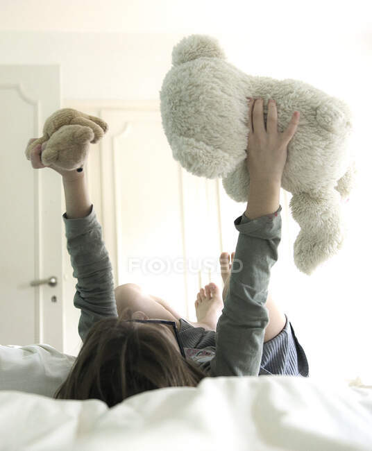 Chica acostada en su cama jugando con dos osos de peluche - foto de stock