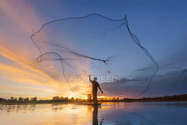 Силуэт рыбака, бросающего рыболовную сеть в реку, Таиланд — стоковое фото