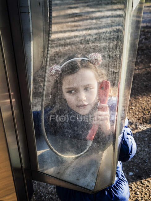 Chica de pie en una cabina telefónica sosteniendo el receptor - foto de stock