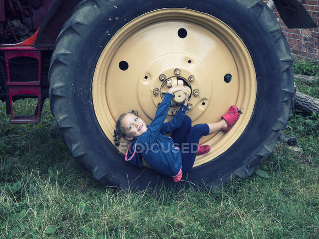 Fille souriante assise sur une grande roue de tracteur dans une ferme, Pologne — Photo de stock