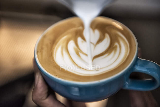 Close-up of a person pouring microfoam on a cup of coffee to make a decorative pattern — Stock Photo