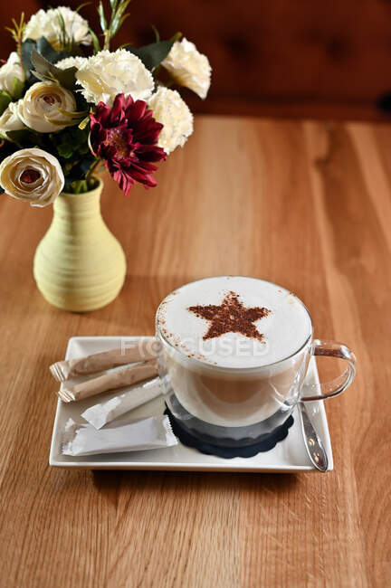 Xícara de café ao lado de um vaso cheio de flores — Fotografia de Stock