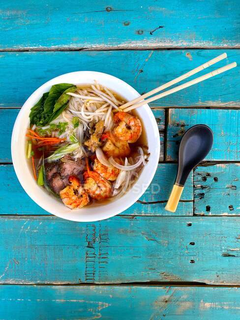 Overhead view of a Vietnamese pho soup with beef and shrimp on a turquoise  painted wooden table — Stock Photo
