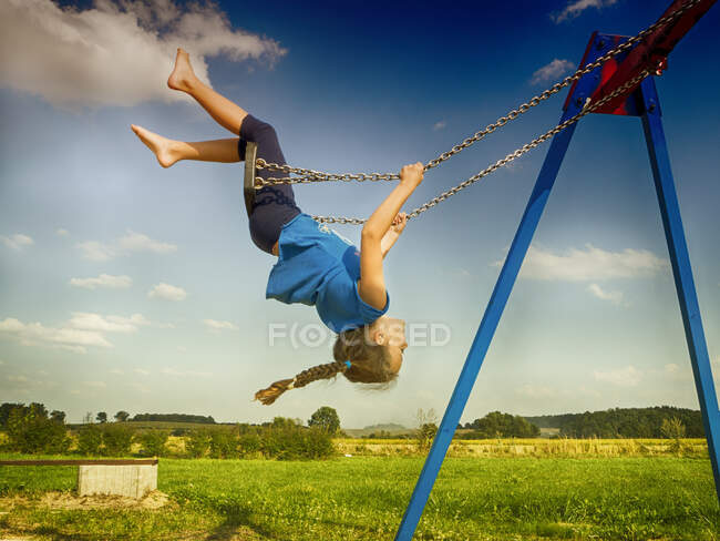 Al revés chica balanceándose en un columpio en un parque infantil, Polonia - foto de stock