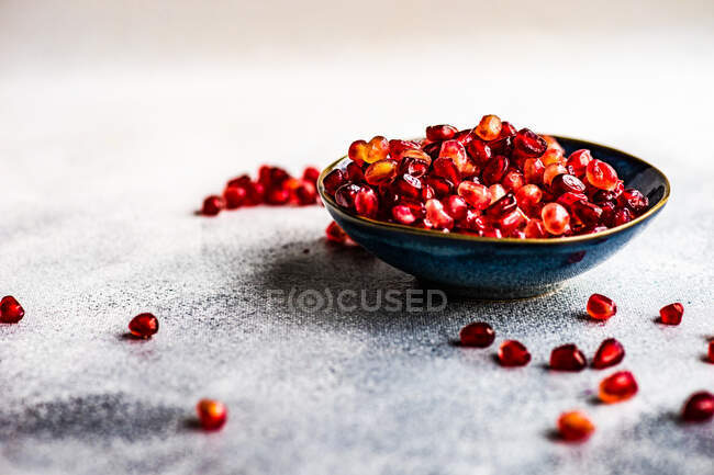 Tigela vermelha e branca de sementes frescas de romã madura em um fundo de madeira — Fotografia de Stock