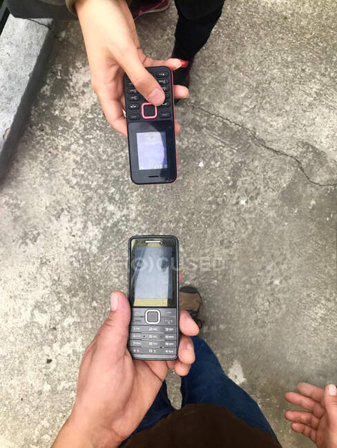 Vista aérea de dos personas sosteniendo teléfonos móviles viejos - foto de stock