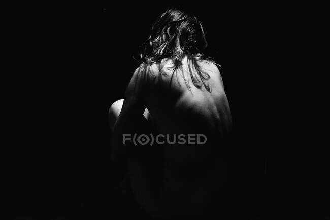 Rear view of a naked woman sitting in the shadows — Stock Photo
