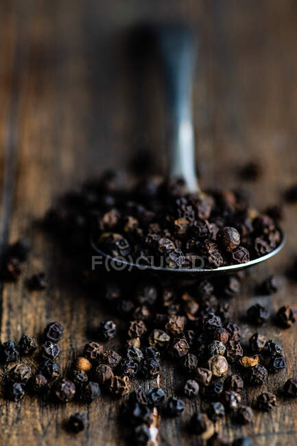 Spoonful of black peppercorns on a  wooden table — Stock Photo
