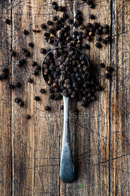 Black pepper in a wooden spoon on a rustic background — Stock Photo