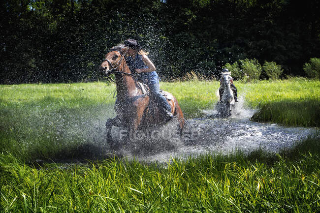 Retrato de mujer y niña cabalgando a través de un lago en el paisaje rural, Polonia - foto de stock
