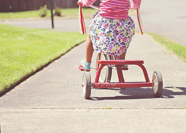 Visão traseira de uma menina pedalando em um triciclo no pavimento, Washington, EUA — Fotografia de Stock