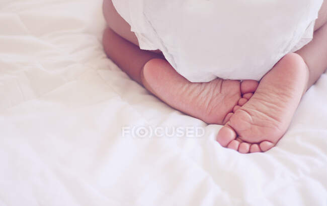 Visão traseira de uma menina em uma fralda ajoelhada em uma cama — Fotografia de Stock
