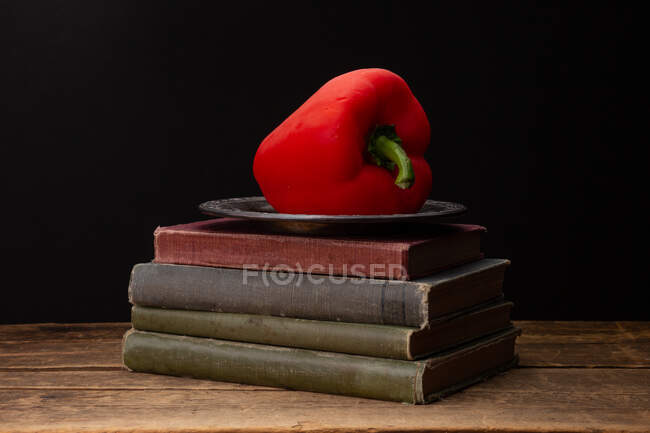 Pimenta de sino vermelha em uma chapa em uma pilha de livros — Fotografia de Stock