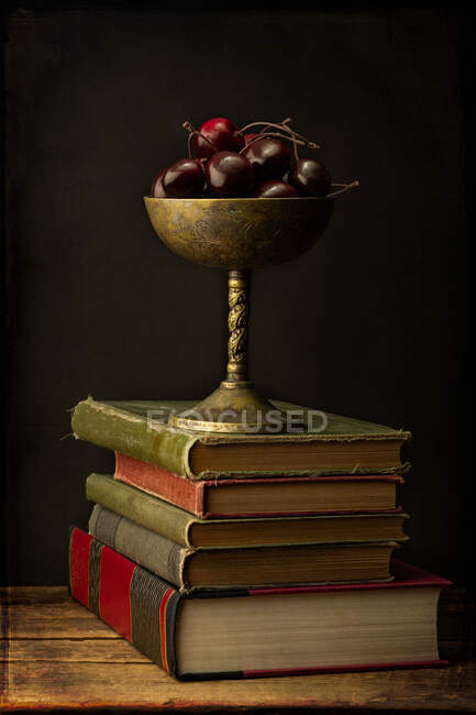 Кубок, наповнений вишнями на стопі книг — стокове фото