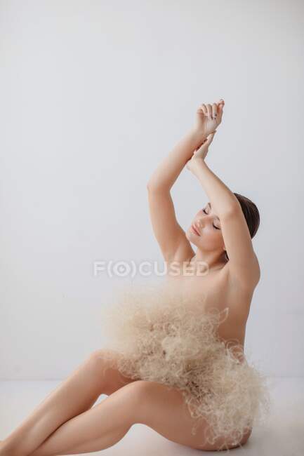 Mujer desnuda sentada en el suelo con un ramo de plantas secas protegiendo su modestia - foto de stock