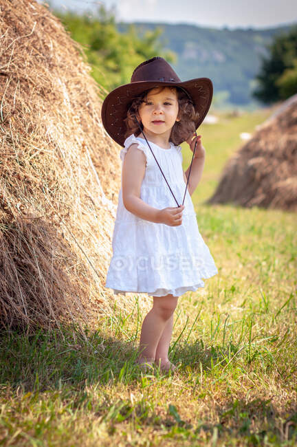 Girl wearing a cowboy hat standing in a field by a hay bale, Bulgaria — Stock Photo