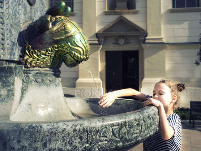 Дівчинка стоїть біля фонтану з водою, тримаючи руку під водою (Угорщина). — стокове фото